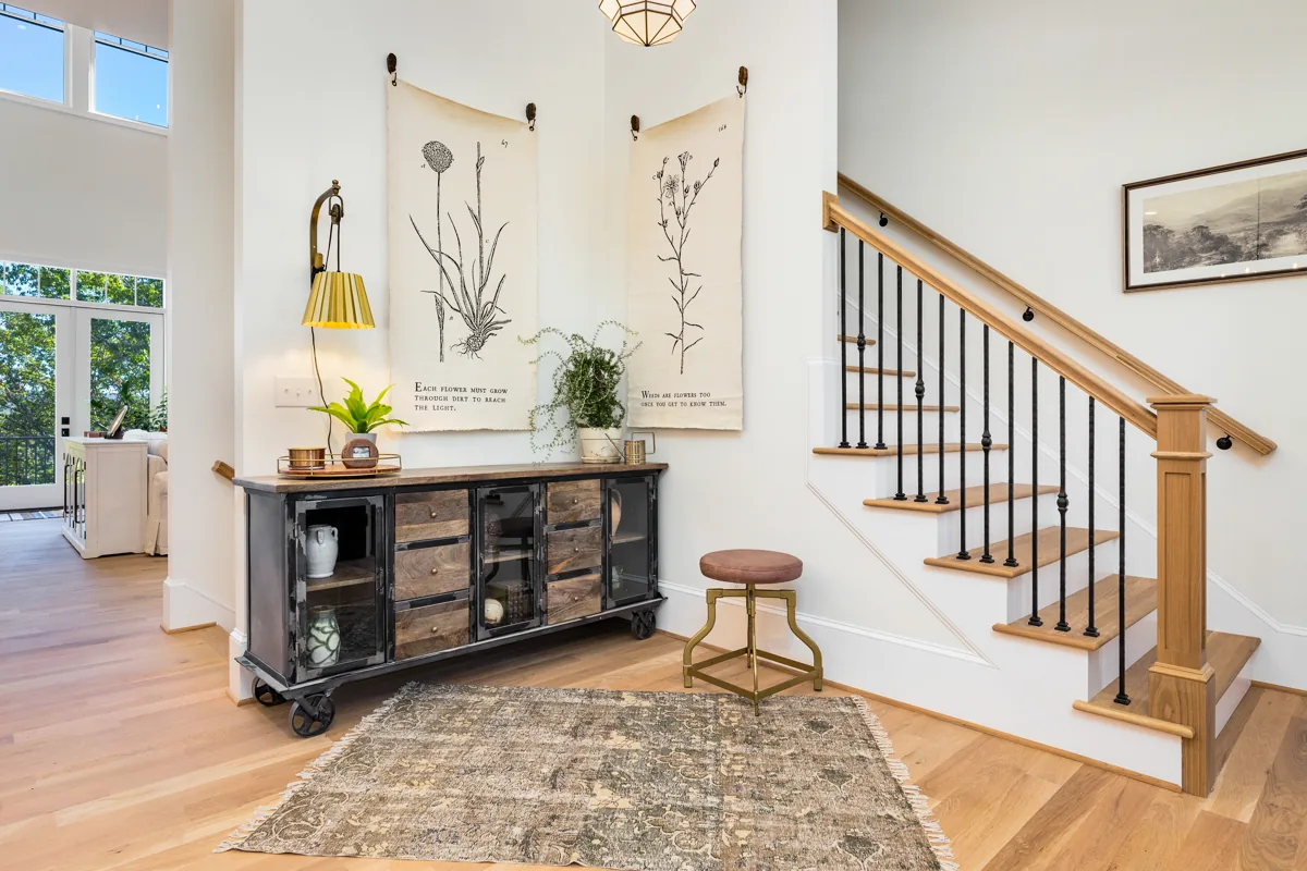 Botanical wall hangings above a dark console beside the wood staircase.