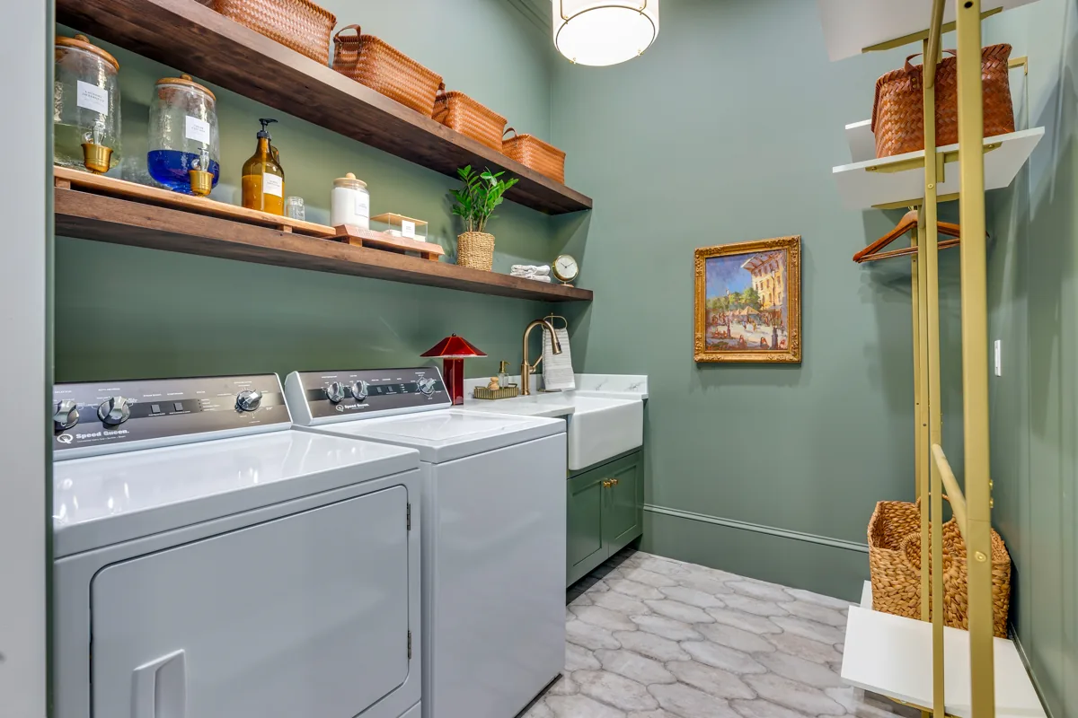 Green walls, open wood shelving, and brass accents in the laundry room.