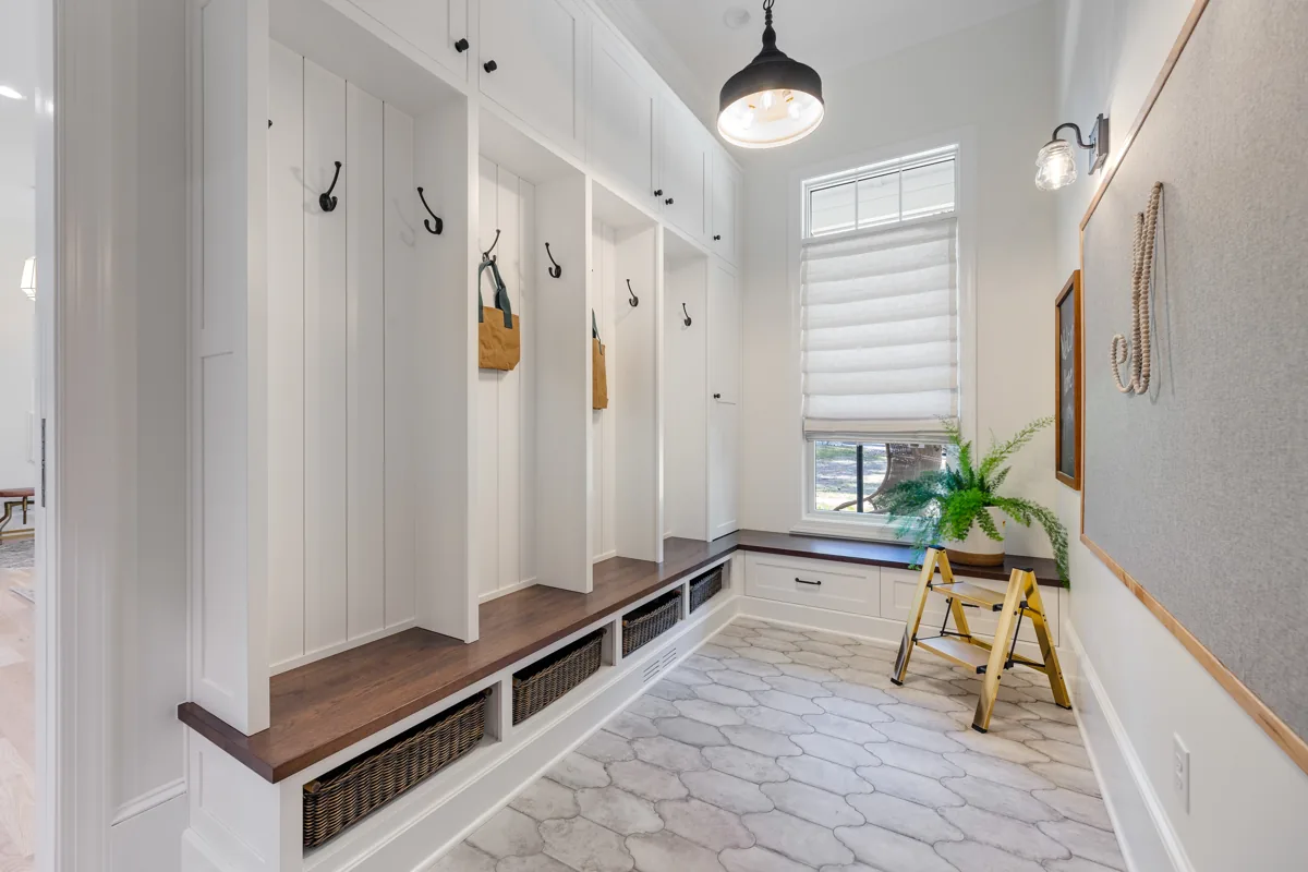 A wood bench, paneled storage bays, and wall hooks beside a sunny window.