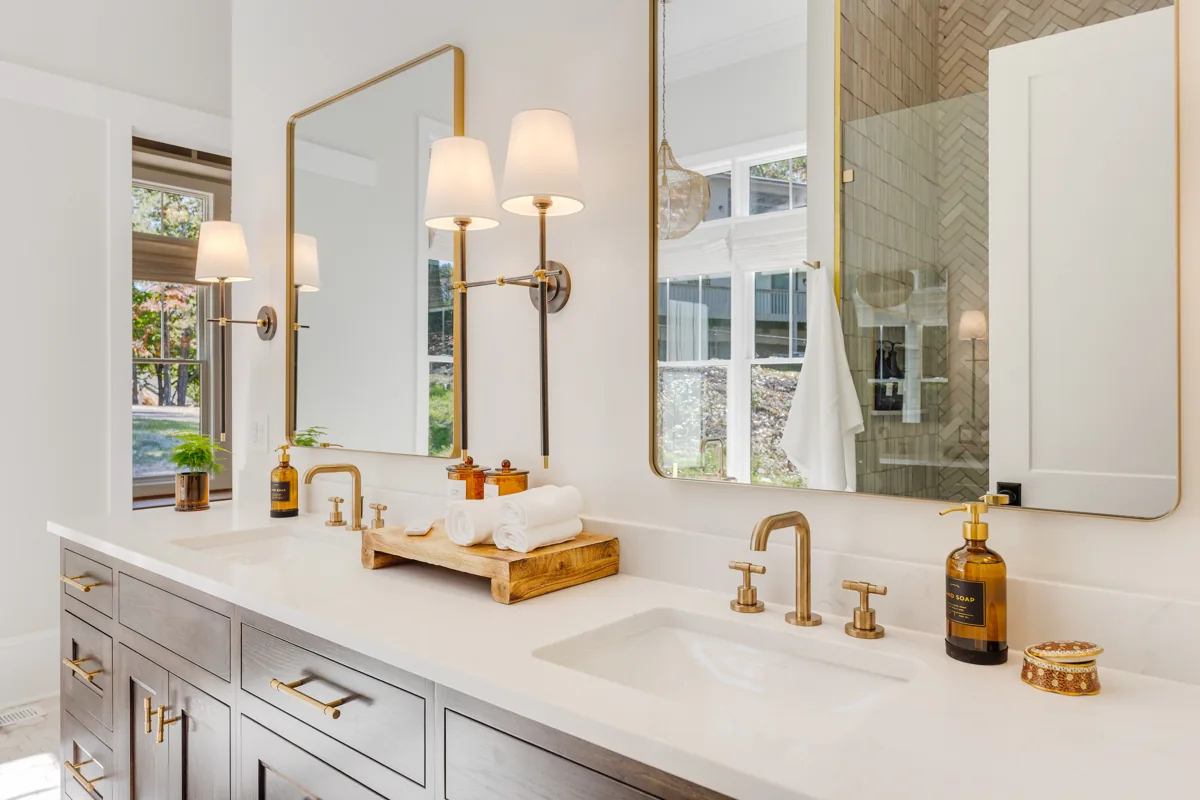 A double vanity with brass fittings, framed mirrors, and warm wall lighting.