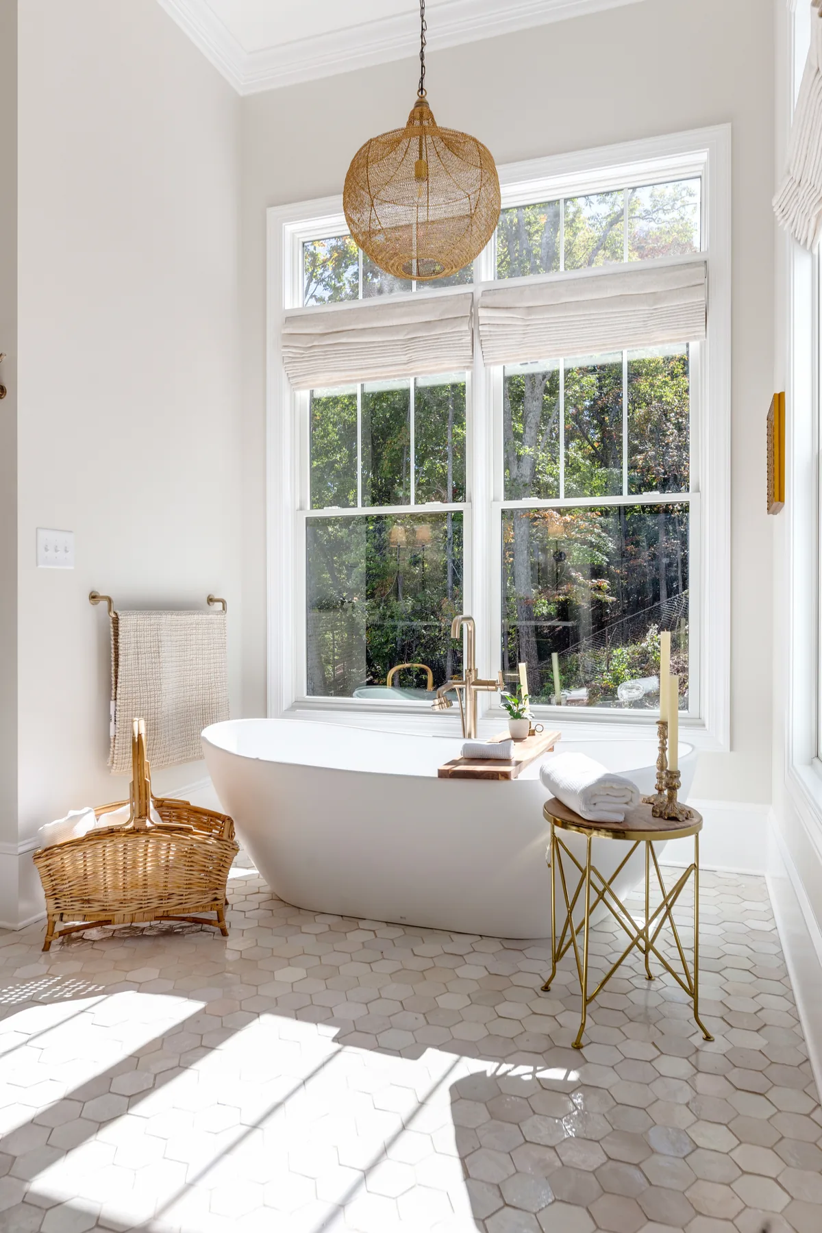 A freestanding tub beneath a woven pendant in a light-filled window alcove.