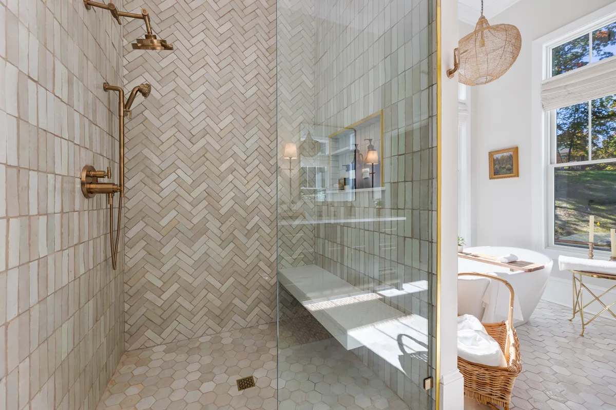 A glass shower with patterned tile and brass fixtures beside the bathing alcove.