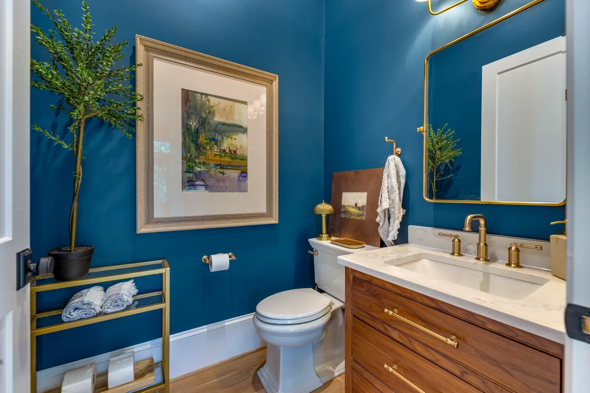 A vivid blue bathroom with a wood vanity, brass fittings, and framed artwork.