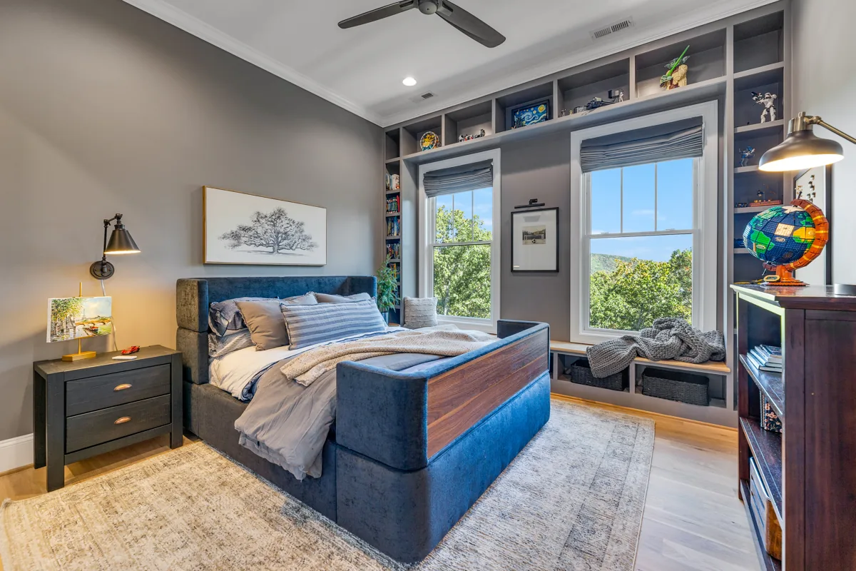 A blue upholstered bed with wood framing, dark walls, and built-in display shelving.