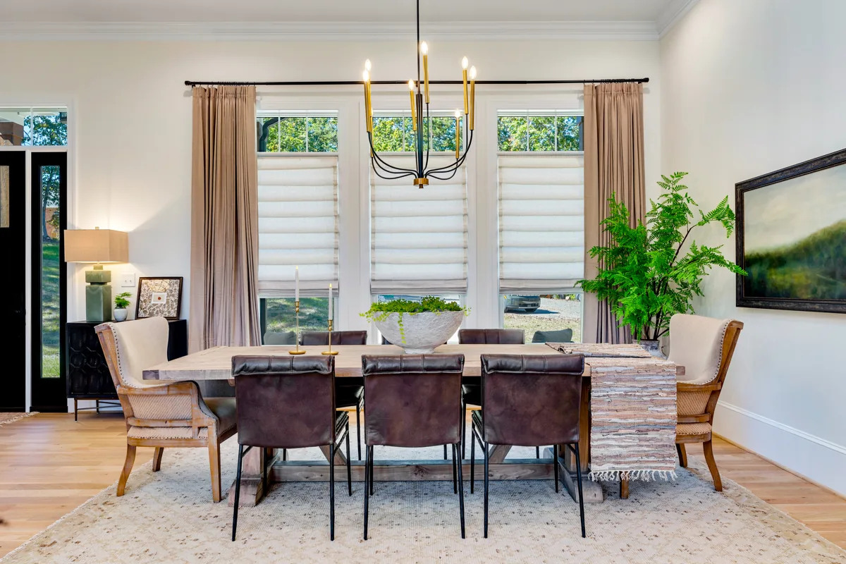 A wood dining table with mixed upholstered chairs beneath a brass chandelier.