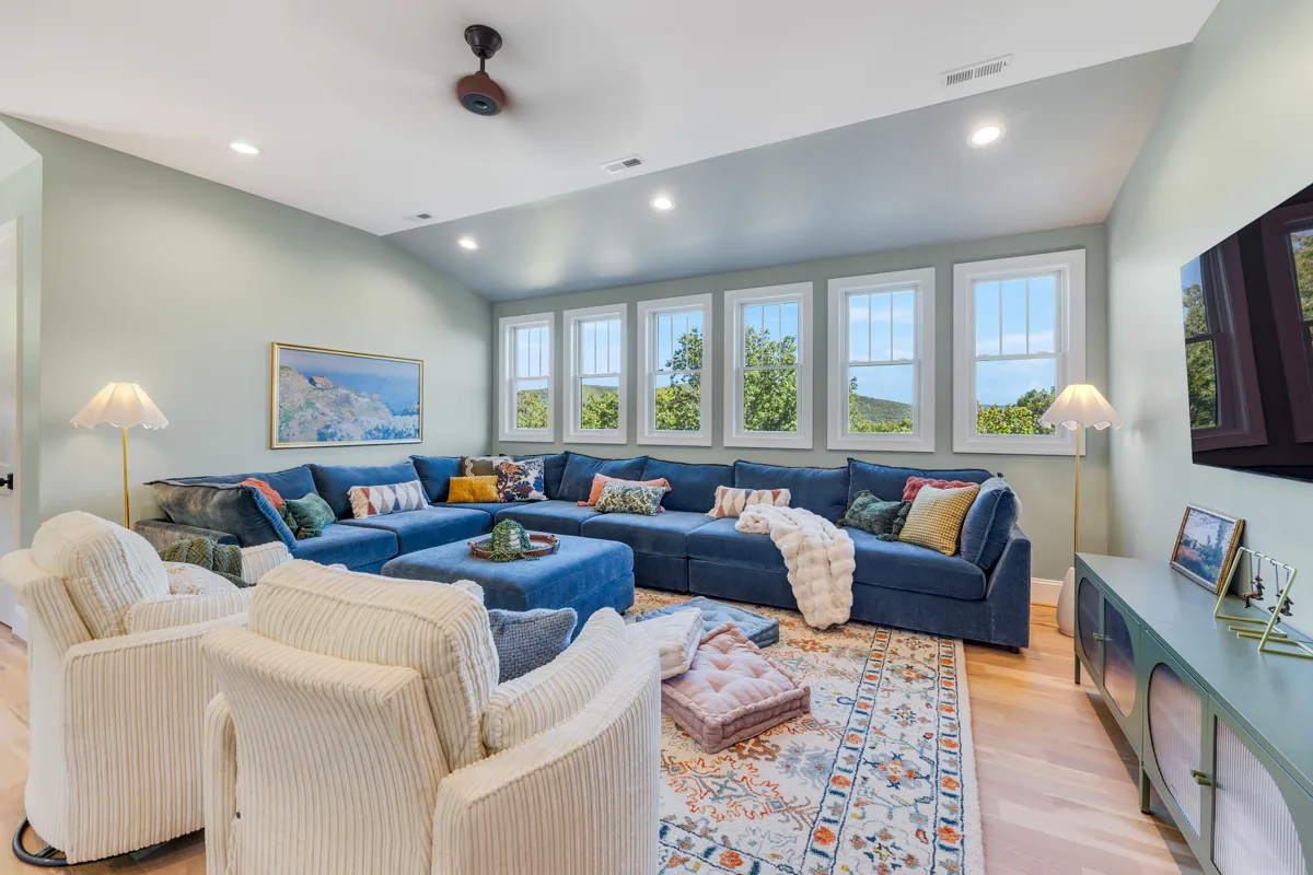 A blue sectional and cream armchairs in a bright room with a colorful rug.