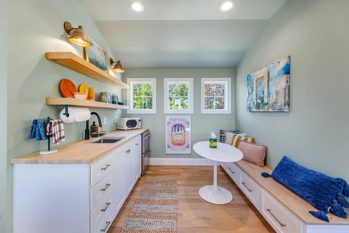 Pale green walls, wood counters, open shelves, and a window-side bench.