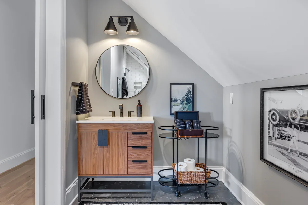 A wood vanity, round mirror, and bold black-and-white patterned floor.