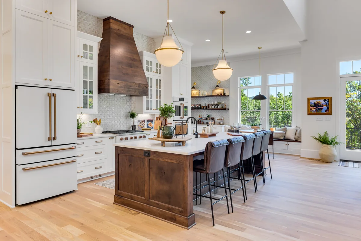 White cabinetry, a wood island and range hood, leather stools, and globe pendant lights.