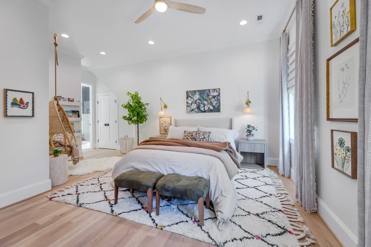 A bright bedroom with warm textiles, a wood bed, wall sconces, and a patterned rug.