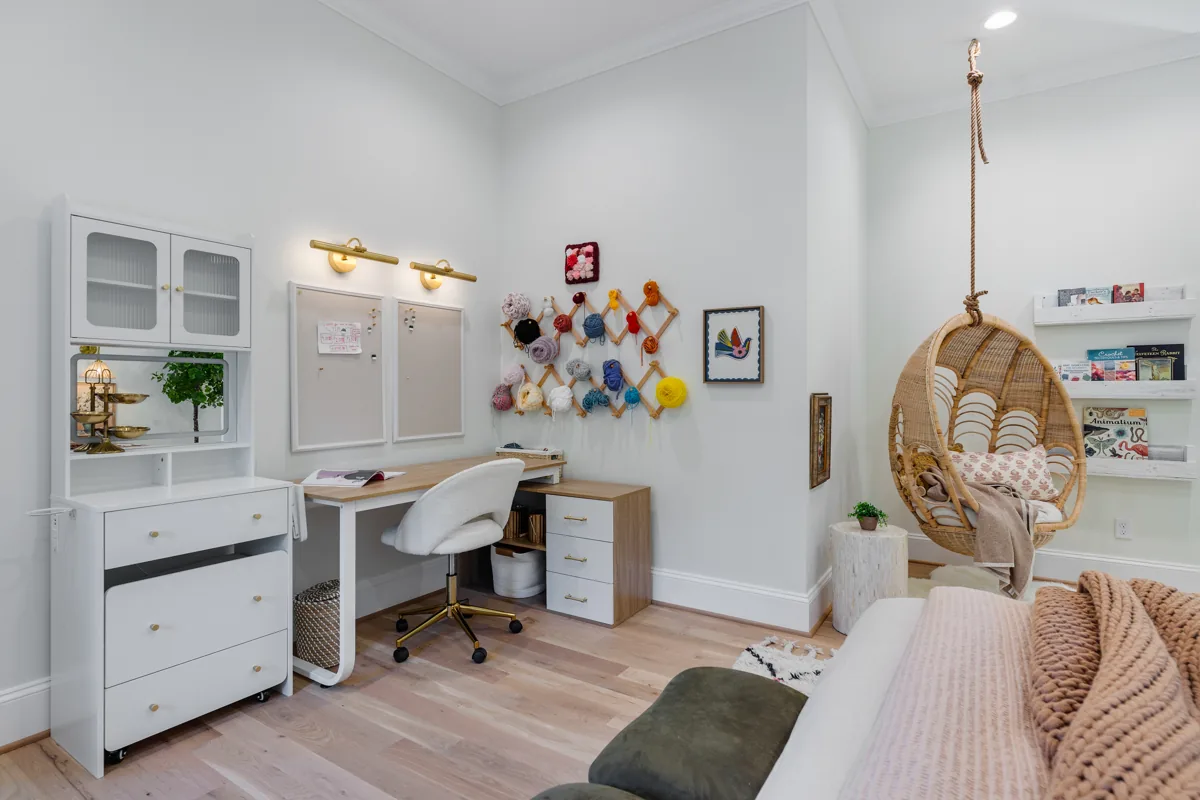 A built-in white desk and cabinets with colorful art and a woven hanging chair.