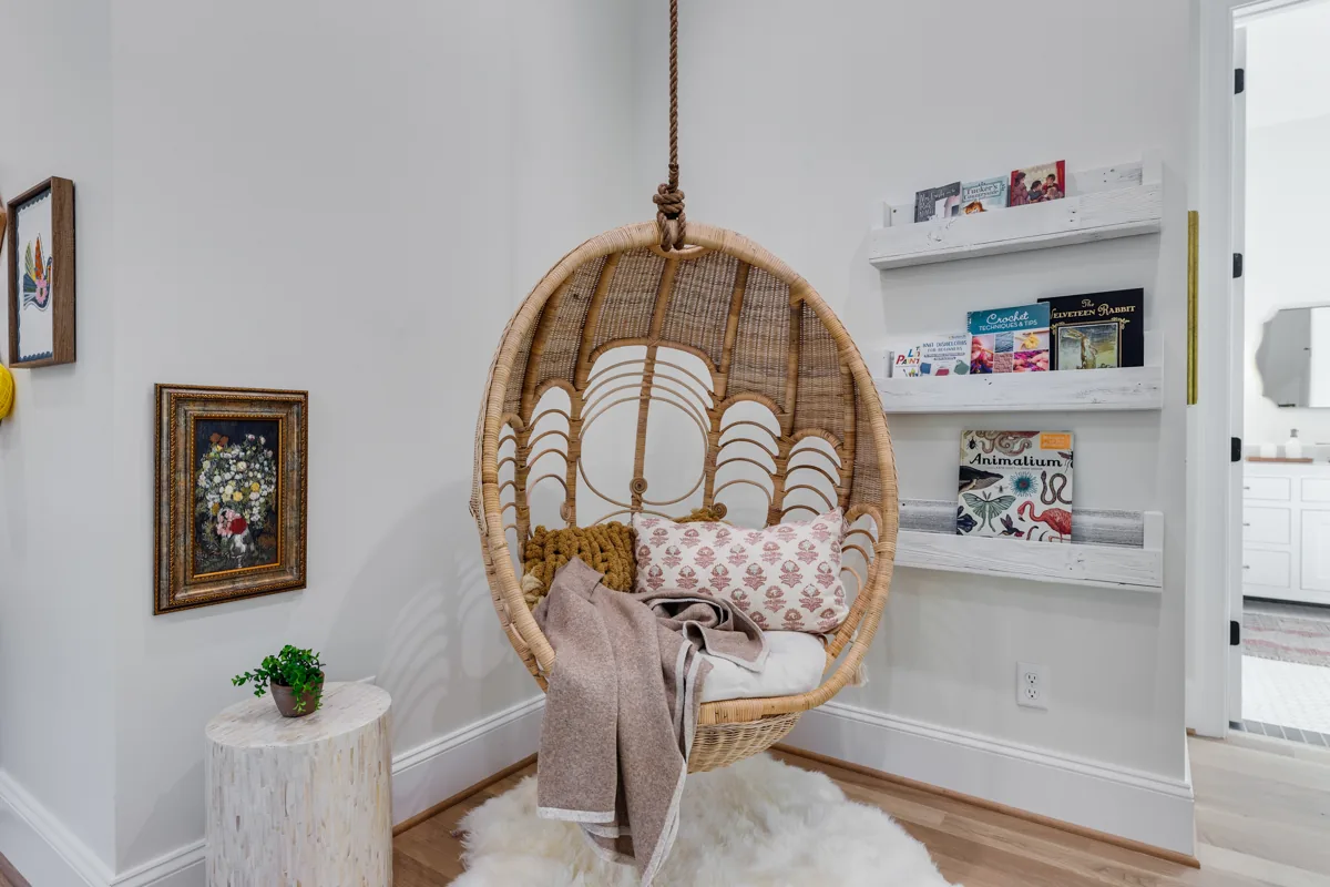 A woven hanging chair and soft cushion beside white shelving and framed art.