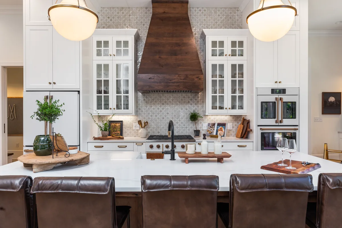 A substantial wood range hood above a patterned backsplash and white counters.